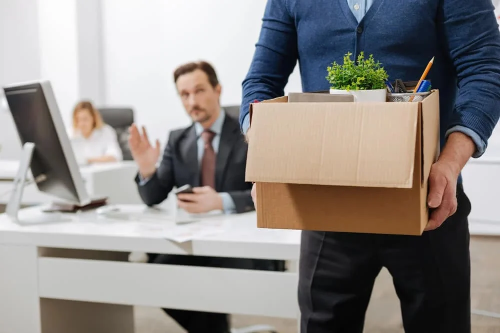 Employee leaving the office with a cardboard box — representing why employees leave and what retaining talent really requires.